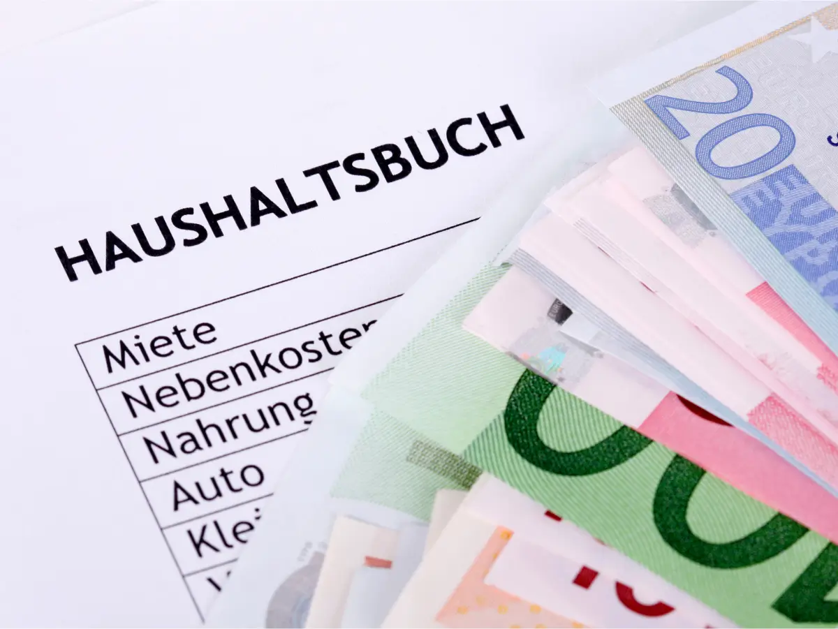 Haushaltsbuchseite mit verschiedenen Ausgaben-Kategorien wie “Miete”, “Nebenkosten”, “Essen”, “Auto” und “Kleidung”. Auf der Seite liegt ein Stapel von Euro-Banknoten, was die finanzielle Verwaltung und Budgetierung im Haushalt symbolisiert. Dieses Bild ist ideal zur Veranschaulichung von Themen rund um Haushaltsplanung, Budgetierung und finanzielle Organisation.